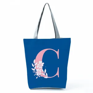 Close-up of blue tote bag with pink initial C letter and floral print, zipper closure style.