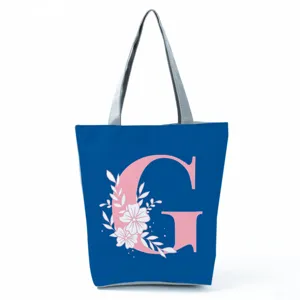 Blue tote bag detail showing pink letter G and white floral print, grey shoulder straps.