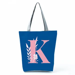 Detailed view of blue tote bag featuring a pink letter K and floral print with grey handles.