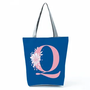 Blue canvas tote bag featuring a pink letter Q and floral print with grey shoulder straps detail.