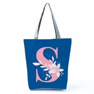 Blue canvas tote bag with pink letter S and floral print, zipper closure and grey straps.