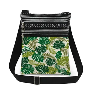 Close-up detail of the double zipper crossbody bag with green tropical leaf print and straps.