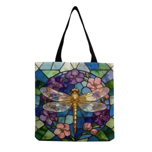Gros plan du sac cabas en toile avec motif de libellule dorée et vitrail floral coloré.