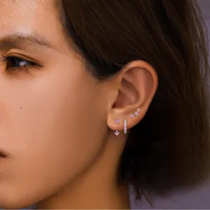 Detailed view of dainty silver-tone purple crystal stud earrings set worn on ear model.