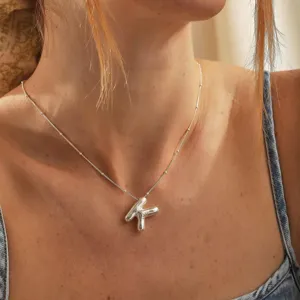 Dettaglio ravvicinato della collana con ciondolo a lettera e catena di perline argentate.