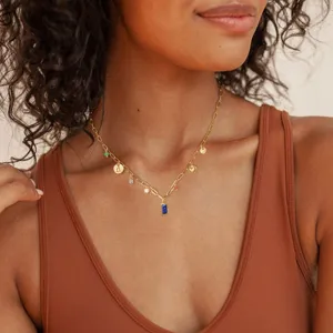 Close-up of elegant gold layered chain necklace featuring blue birthstone pendant charm.