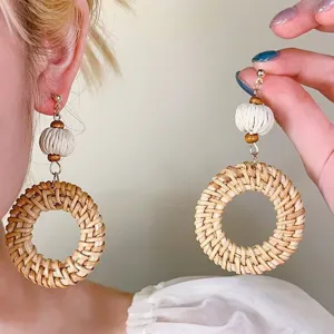 Close-up detail van handgemaakte rotan geweven geometrische oorbellen met houten kralen.
