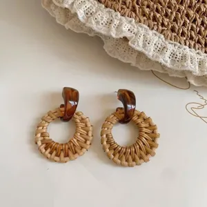 Gedetailleerde close-up van rotan geweven geometrische oorbellen met amberkleurige knopjes.