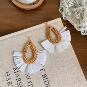 Gedetailleerd uitzicht van zomerse rotan oorbellen in druppelvorm met witte franjes, chic.