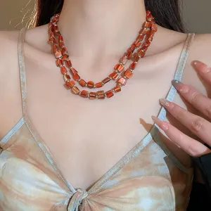 Nahaufnahme Detail der mehrlagigen orangen Muschelperlen Kette mit goldenen Kugeln am Hals.