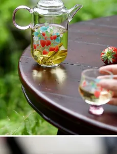 Detailed view of clear borosilicate glass teapot with charming strawberry pattern and pink handle.
