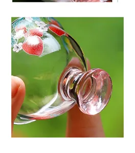 Close-up detail of clear glass tea cup featuring cute red strawberry and white flower painted design.