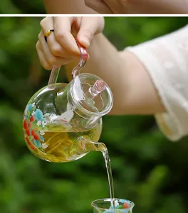 Detail shot of a clear glass teapot featuring cute strawberry floral prints pouring tea.