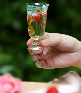 Primer plano detalle de una taza de té de vidrio de tallo alto con fresas en la naturaleza.