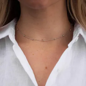 Primo piano dettaglio di una delicata collana girocollo di perle argentate al collo.