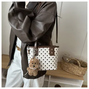 Detailaufnahme einer weißen Eimer Tasche mit Punkten, braunem Besatz und Plüschhunde Anhänger.