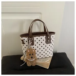 Stilvolle Pünktchen Eimer-Tasche Detail mit braunen Griffen und einem süßen Plüsch-Hund-Anhänger.