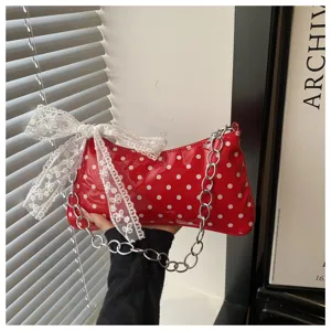 Detail van de rode schoudertas met polka dots, kanten strik en metalen ketting.