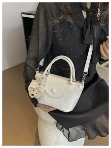 Gedetailleerd overzicht van witte lakleren handtas met berensleutelhanger en schouderband.