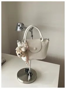 Witte leren handtas detail met gekreukte textuur, klep en schattige berensleutelhanger.