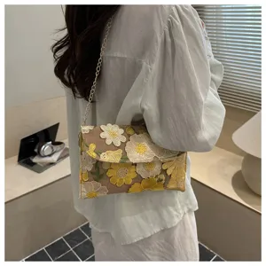 Detailed shot of a floral embroidered shoulder bag with chain strap in a cozy room setting.