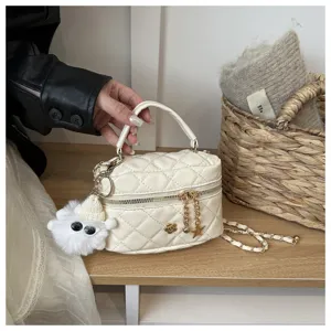 Detalle de bolso vanity acolchado blanco con correa de cadena dorada y tierno colgante de peluche.