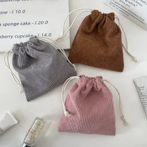 Three corduroy drawstring cosmetic bags in pink, brown, and gray shown on a desk