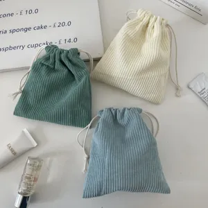 Close-up of three colorful corduroy drawstring storage pouches in green, cream, and blue