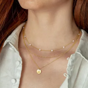 Gedetailleerd overzicht van de gelaagde gouden ketting met parels en letter hanger.