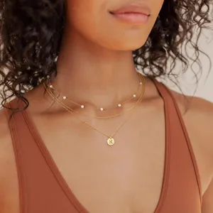 Gedetailleerde close-up van een meerlaagse goudkleurige ketting met parels en letter K hanger.