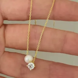 Elegant gold chain necklace featuring a delicate pearl and sparkling solitaire pendant.