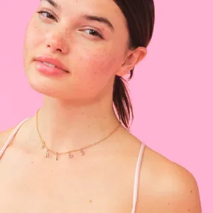 Close-up detail of a delicate gold chain necklace featuring alphabet letter charms worn by a model.