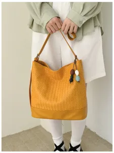 Stylish yellow woven bucket bag with leather bottom and cute hanging charms for summer.