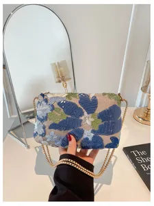 Elegante schoudertas met pailletten en blauw bloemenborduurwerk en chique gouden ketting.