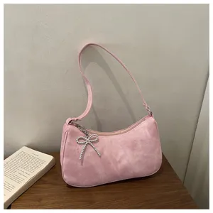Pink matte underarm shoulder bag with delicate beaded bow pendant, textured minimalist design.