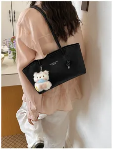 Detailed shot of a stylish black shoulder bag with a cute plush bear pendant, large capacity.