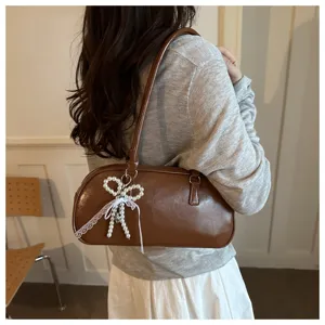 Detail view of a chic brown leather shoulder bag featuring a pearl bow and lace accent.