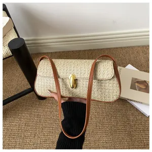 Détail du sac baguette en paille avec texture tissée, lanière en cuir et serrure dorée.