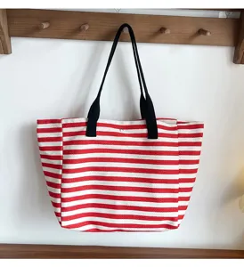 Detailed view of red and white striped canvas tote bag hanging on wooden wall hook.