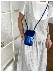 Glossy vertical phone crossbody bag detail, modern minimalist style accessory in deep blue.