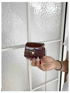 Close-up detail of a mini glossy croc-embossed crossbody bag with gold chain strap in hand.