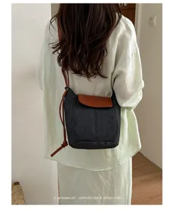 Bolso cubo minimalista de mezclilla para mujer con solapa de cuero marrón y correa.