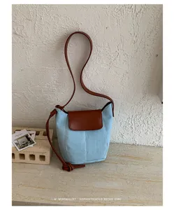 Vista de cerca de un elegante bolso tipo cubo de denim con solapa de cuero marrón y correa.