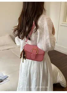 Pink fabric shoulder bag detail featuring metallic buckle and wooden bead charm pendant.