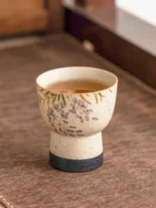 Close-up of ceramic high-foot tea cup with hand-painted wisteria and gold detail for tasting.