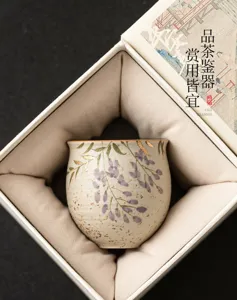 Hand-painted ceramic tea cup detail featuring delicate wisteria flowers and gold trim inside a gift box.