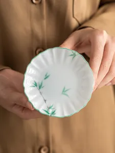 Close-up detail of the hand-painted green bamboo ceramic tea coaster and floral dish.