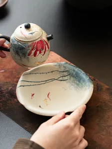 Hand-painted ceramic tea saucer and teapot set with lotus and koi fish detail design.