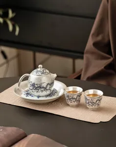 Zilververgulde theeservies detailopname met traditionele drakenpatroon theepot op mat.