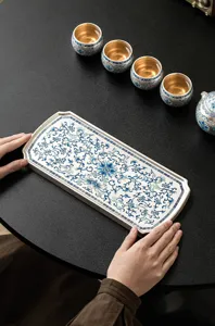 Vista dettagliata del vassoio da tè in ceramica argentata con motivo floreale blu su tavolo nero.